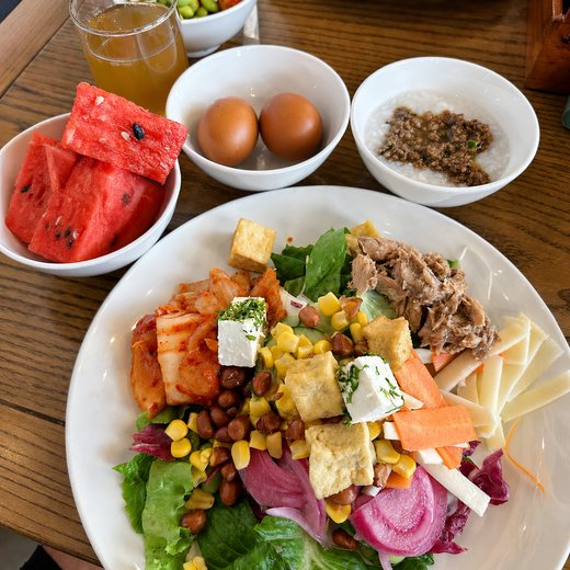 A full breakfast spread: salad, watermelon, soft-boiled eggs, congee and fresh juice.